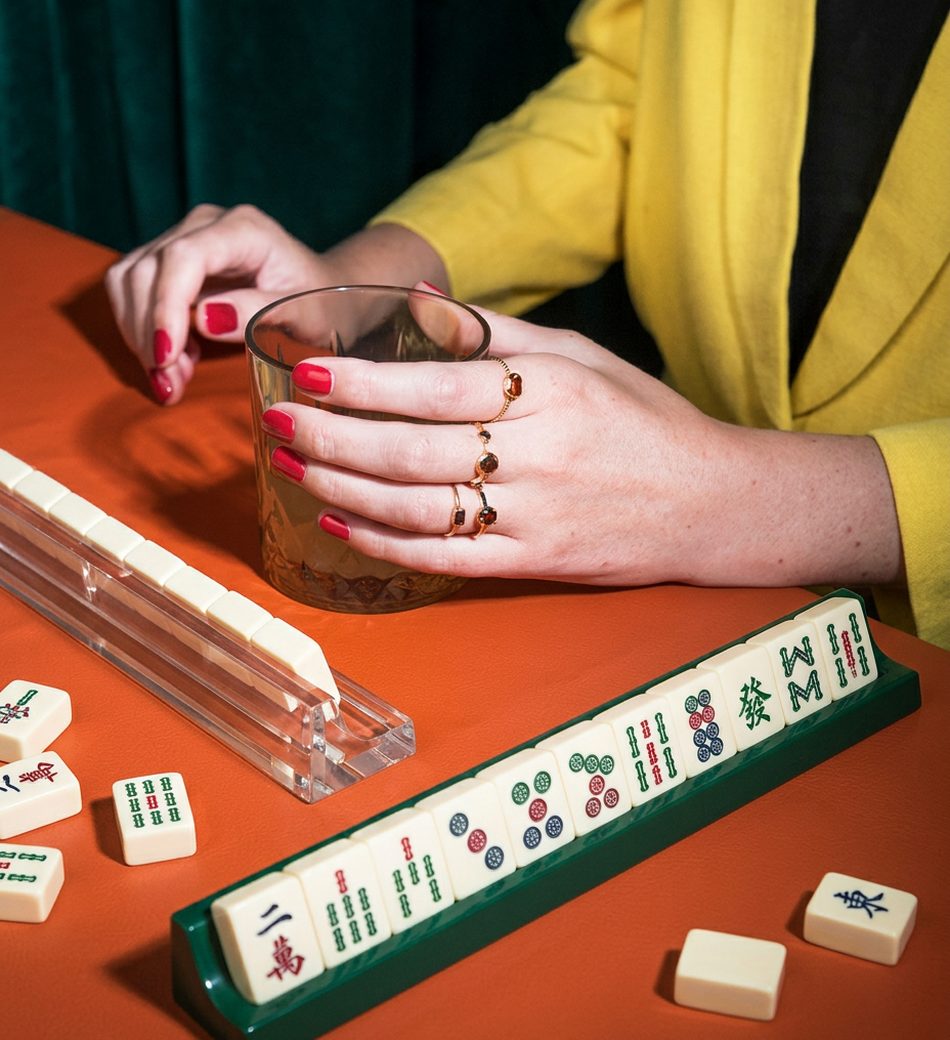 A player reaching for a tile beside a drink at a mahjong table